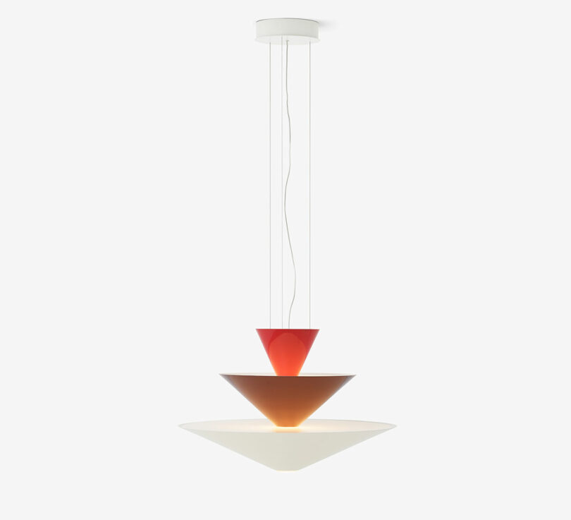 A modern pendant light with three tiered conical shades in red, brown, and white, suspended by wires from a circular ceiling mount.