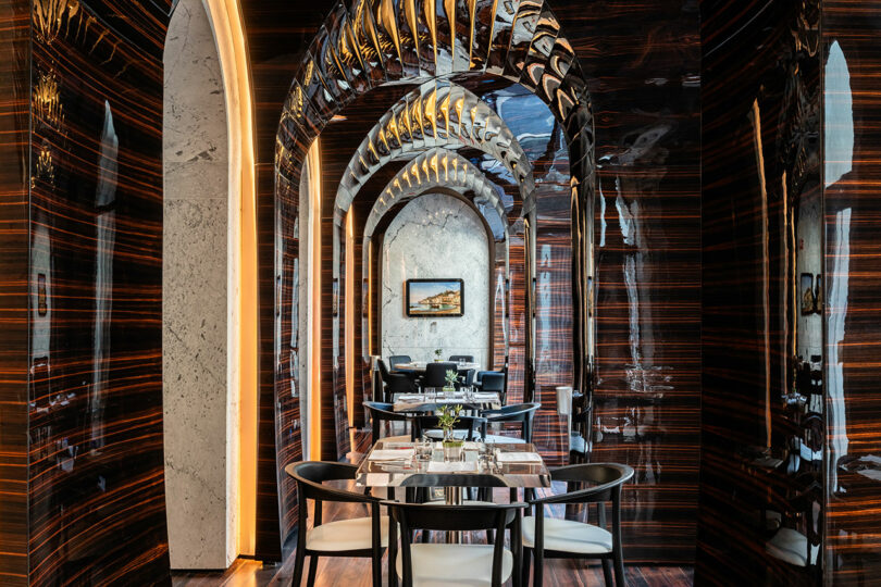 Elegant restaurant interior with dark wood-paneled walls, arched ceilings, and tables set for dining. A framed picture hangs on a wall, enhancing the sophisticated ambiance.