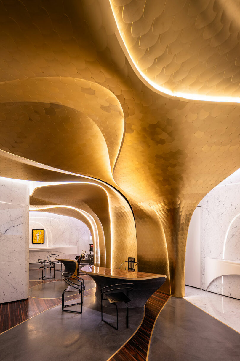 A modern interior with a gold, sculptural ceiling resembling scales, marble walls, and sleek black furniture. The design features curved elements and ambient lighting.