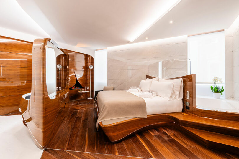 Luxurious modern hotel room with polished wood furnishings, a large bed, a sleek design featuring smooth curves, and ambient lighting.