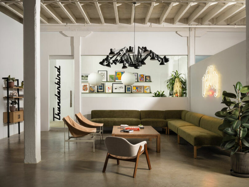 Modern lounge area with green sectional sofas, wooden chairs, a geometric chandelier, and wall art. Neon 