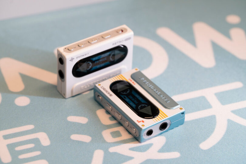 Two compact retro-style cassette players in white and blue rest on a light blue surface with white text.