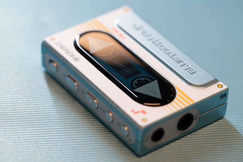 Portable cassette player with buttons on the side, a display screen, and a headphone jack on a blue surface.