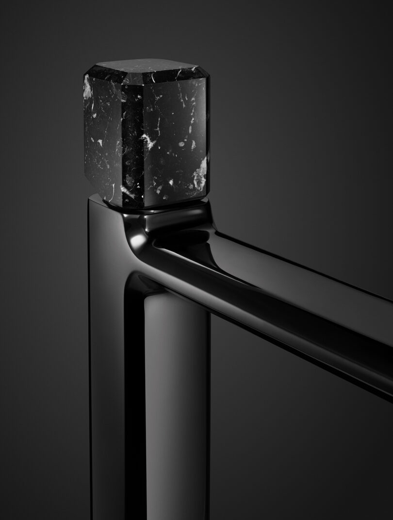 Close-up of a modern black railing with a glossy finish, featuring a square marble cube on top against a dark background.
