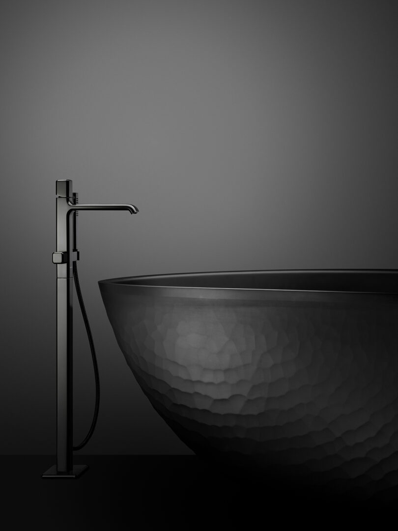 A minimalist bathroom features a black freestanding faucet next to a textured, round black bathtub against a dark gray background.