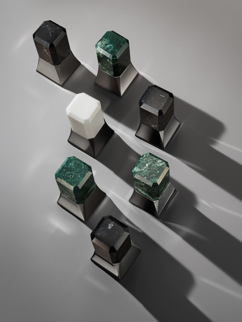 Hexagonal stone objects with various colors, including black, green, and white, on black bases casting long shadows on a gray surface.