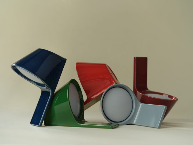 Four modern tile lamps in blue, green, red, and gray with unique, angular designs are arranged on a neutral background