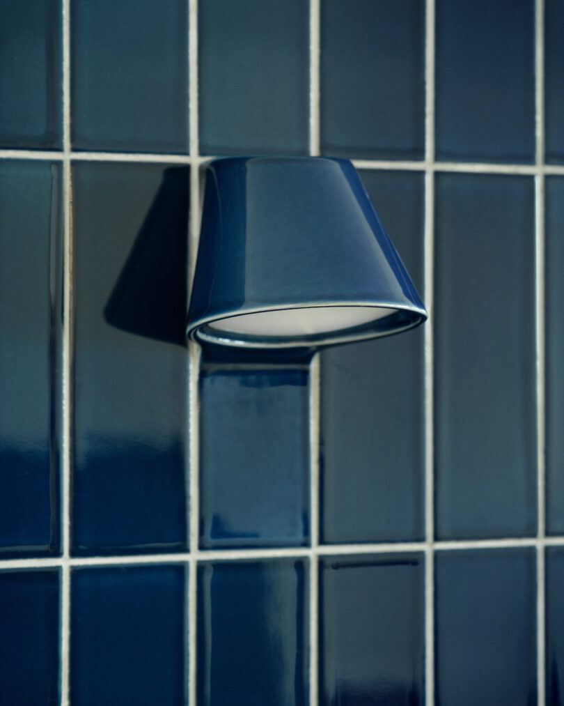 Blue ceramic wall sconce on a grid of glossy dark blue tiles