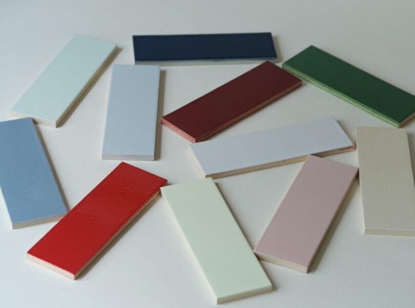 An arrangement of rectangular, colorful tile samples in various shades, including red, green, blue, and beige, scattered on a white surface