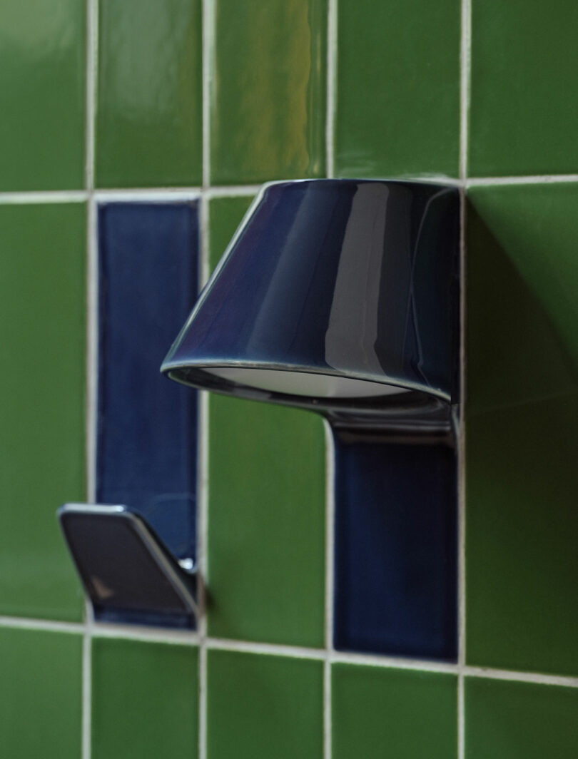 Dark green and blue ceramic wall-mounted water spout and control lever against a green tile background, featuring elegant UU Tiles for a touch of sophistication.