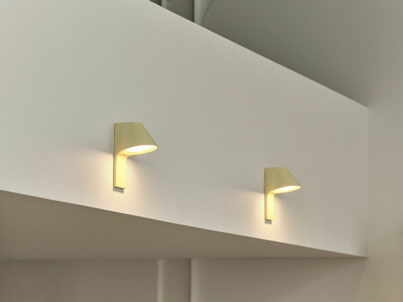 Two modern wall-mounted lamps emit a soft glow on a light-colored wall, beautifully highlighting the elegant texture of UU Tiles.