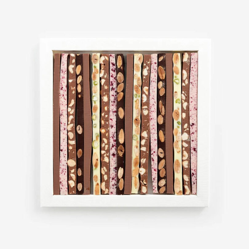 A white square frame displays vertical rows of assorted chocolate bars with visible nuts and fruit pieces in various colors and flavors.