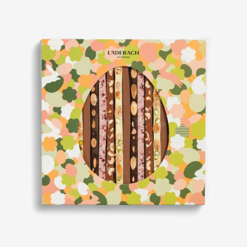 A box of Läderach Swiss chocolate sticks with assorted toppings, displayed in a floral-patterned packaging with an oval window.
