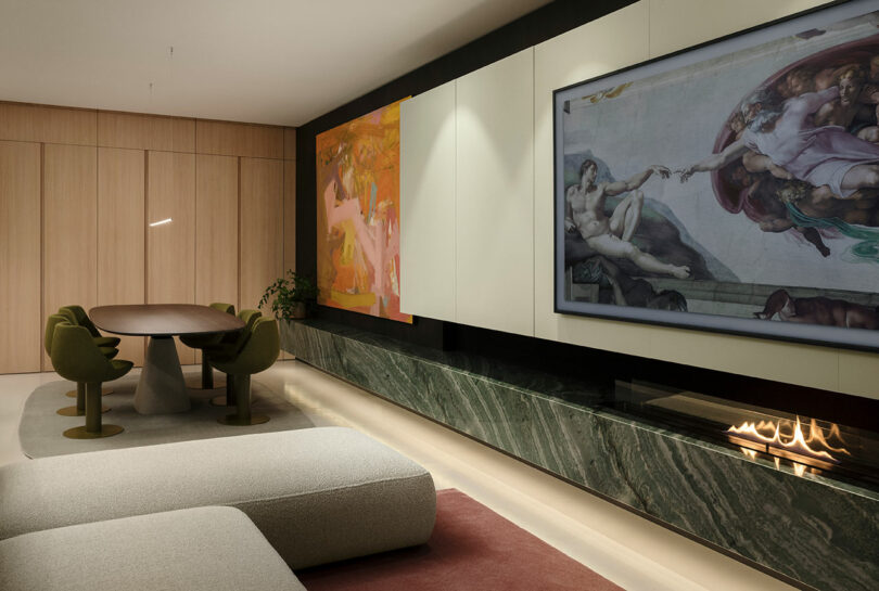Modern living room with a large wall-mounted screen displaying art, a long green marble fireplace, a wooden dining table, green chairs, and light-colored sofas.