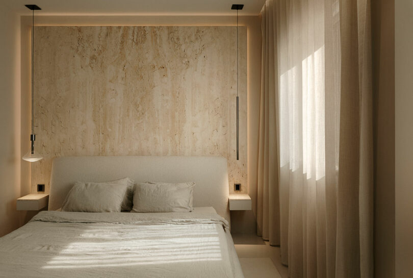 Modern bedroom with a beige theme, featuring a double bed, textured accent wall, hanging lights, and sheer curtains allowing natural light to filter in.