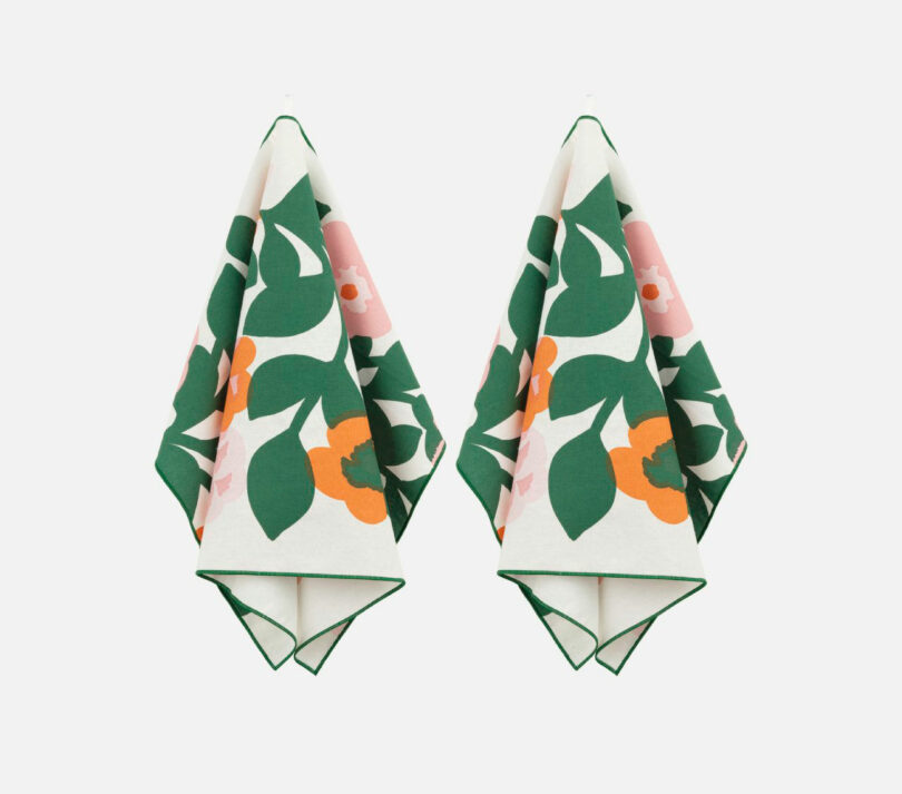 Two hanging towels by Elizabeth Rees showcase a stunning floral pattern with green leaves and orange and pink flowers on a crisp white background.