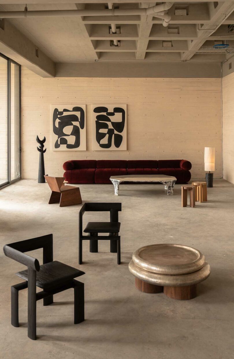 A modern, minimalist living room with abstract art on the wall, a red sofa, and various unique chairs and tables on a concrete floor