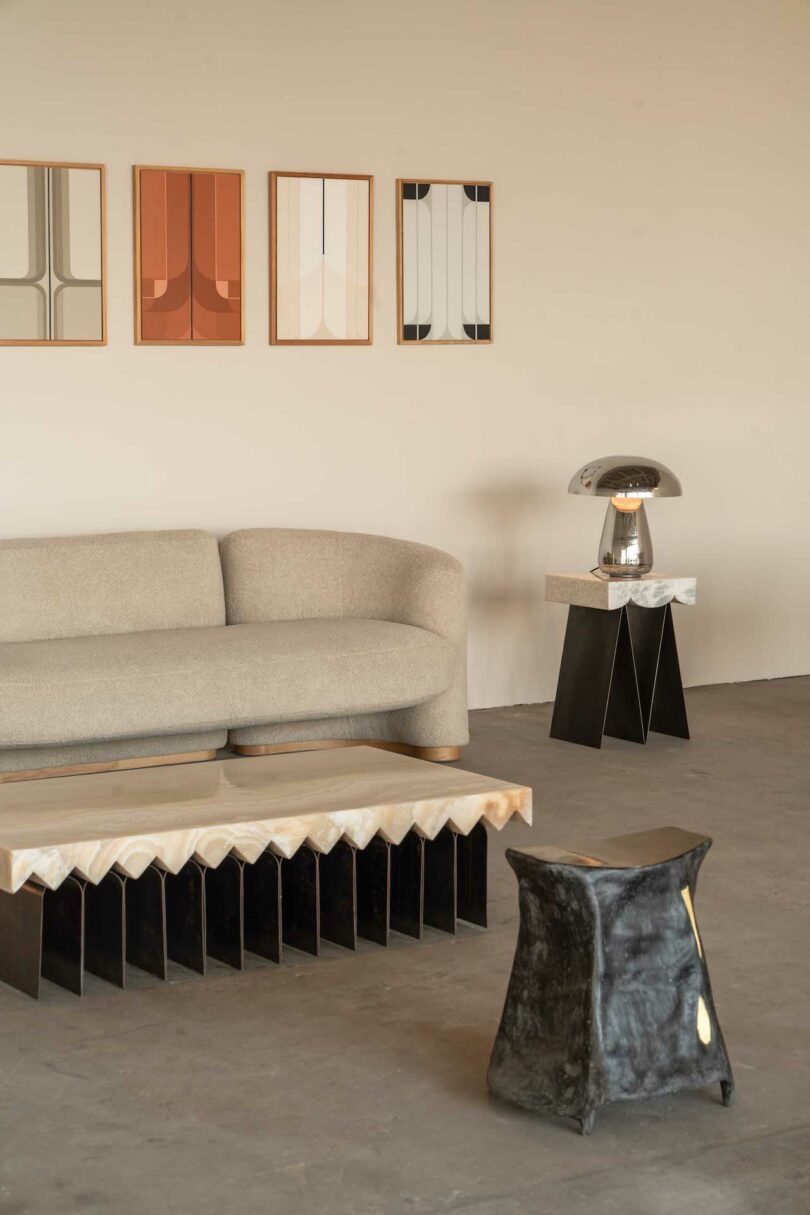 Minimalist living room with a curved beige sofa, abstract artworks on the wall, a geometric coffee table, and a modern lamp on a side table