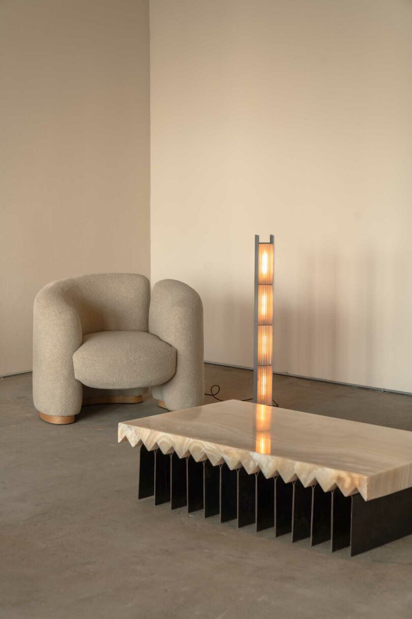 A beige armchair, a wooden table with a jagged edge, and a vertical lamp with multiple light segments in a minimalistic room