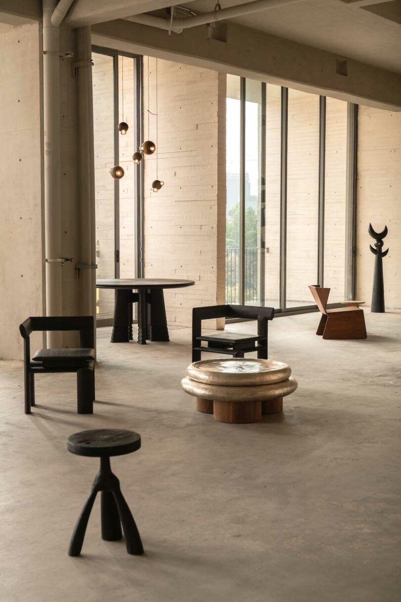 Spacious, minimalist interior with concrete floor, featuring modern black and wooden chairs, round table, pendant lights, and large windows