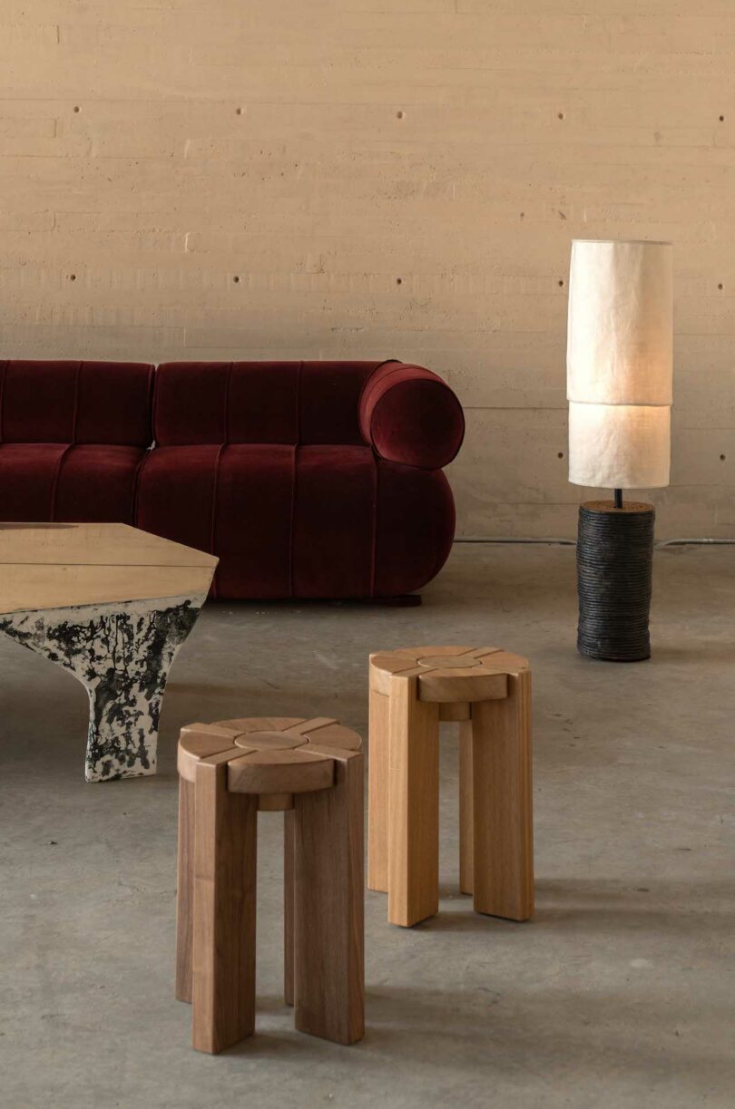 A minimalist room with a red sofa, two wooden stools, a textured coffee table, and a white floor lamp
