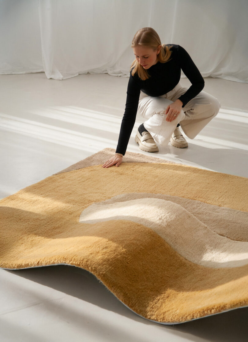 Person in a black top and white pants examines a textured beige and tan chaise/rug hybrid 