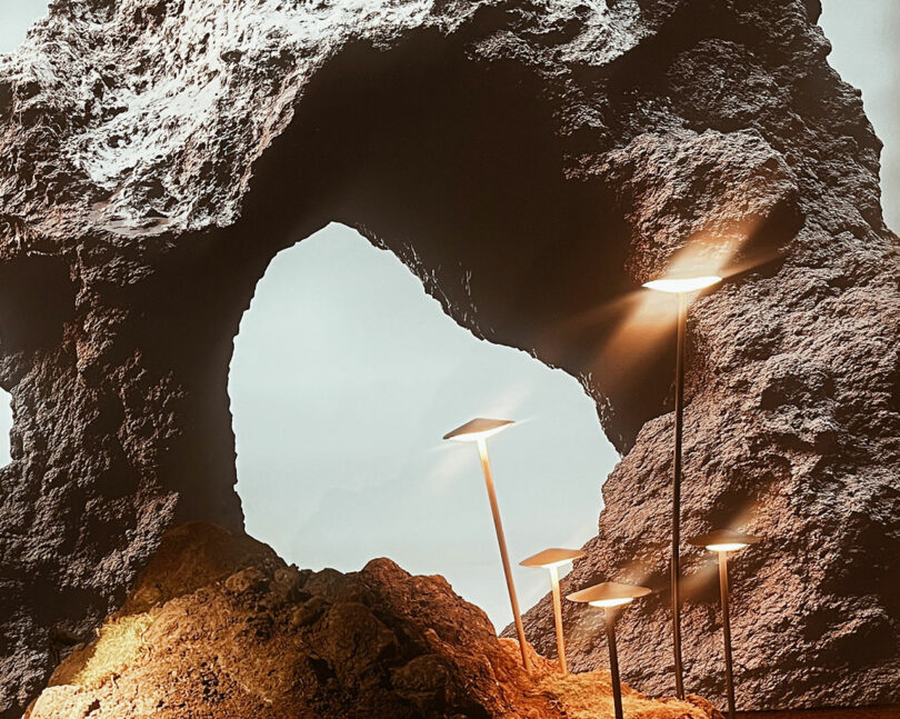 Rock formation with a natural arch in the background and several modern, square-shaped lights on tall poles illuminating the foreground.