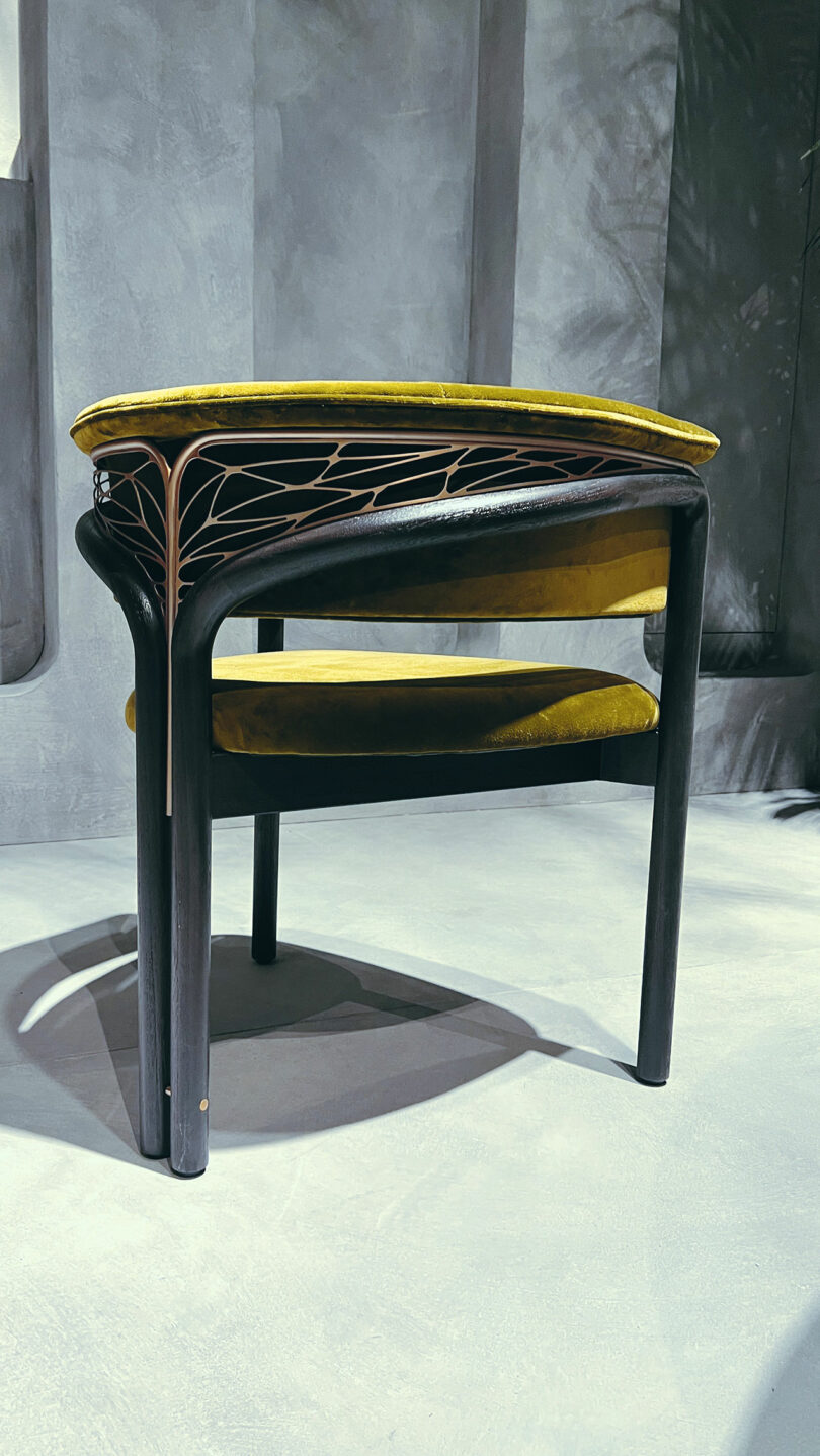 A modern chair with a dark wooden frame, yellow upholstered seat and backrest, and a decorative metal accent on the side, set against a gray, textured background.