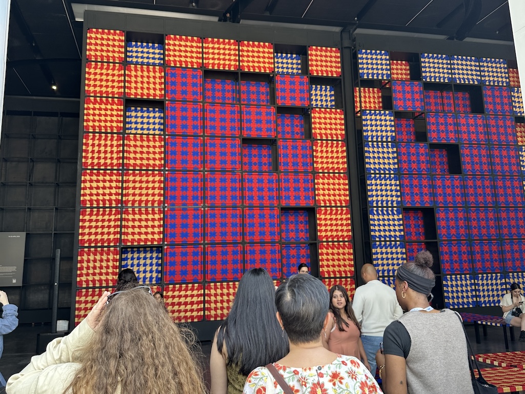 How-Alserkal-Avenue-Became-the-Beating-Heart-of-Dubais-Art.jpg People gaze at a 25-foot tall installation made of woven squares in red, blue, and gold.