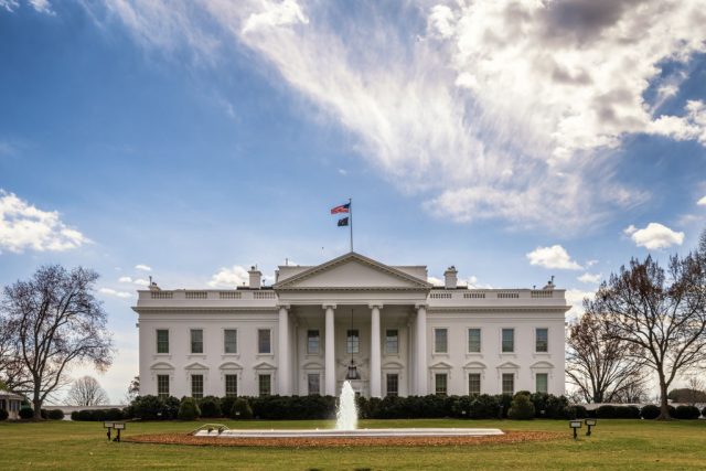 A white columned building with a fountain in front of it.