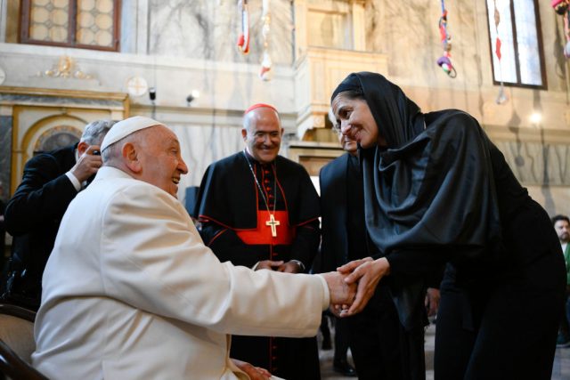 A man in papal robes greeting a woman in a black headscarf.