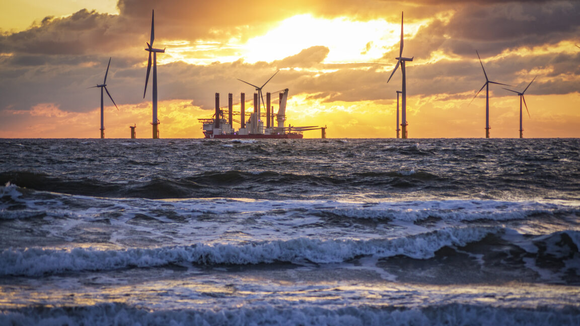 US-Interior-secretary-orders-offshore-wind-project-shut-down.jpg gentle waves are in the foreground, was a ship sits among wind turbines, carrying the parts for additional ones.