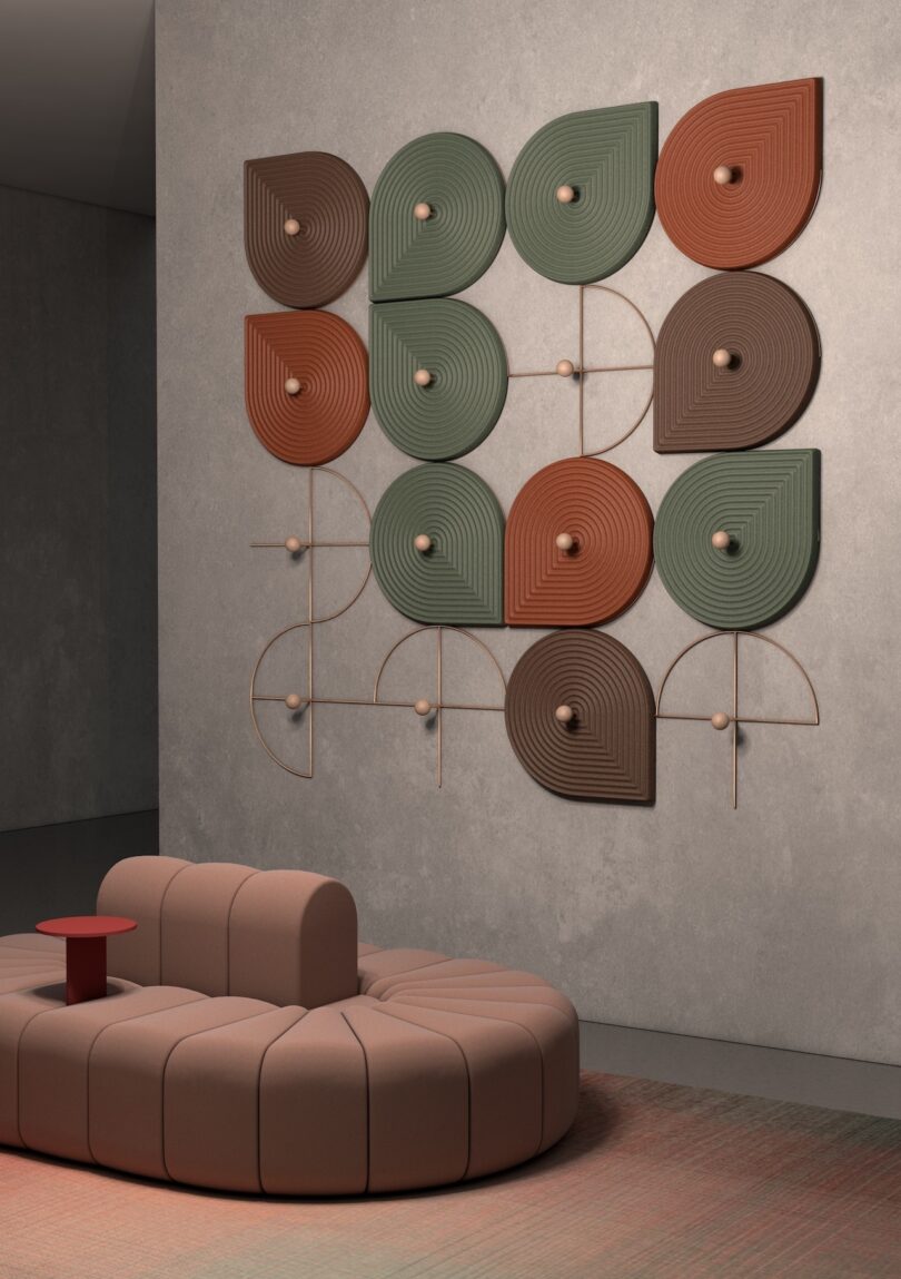 Geometric wall art with green, brown, and orange shapes hangs above a rounded, modular beige sofa on a multicolored carpet in a modern, minimalist room