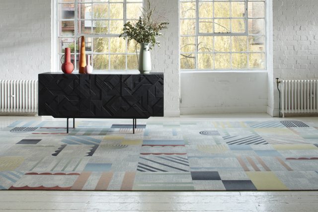 1747679587_Presenting-Clerkenwell-Design-Week-Product-Awards-Winners.jpg Colorful geometric carpet tiles in a bright room with a black textured sideboard and large windows.