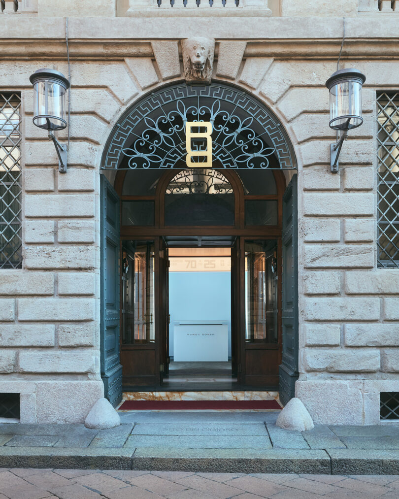 Arched stone entrance with glass doors, metal lanterns, decorative ironwork, and a modern sign reading 