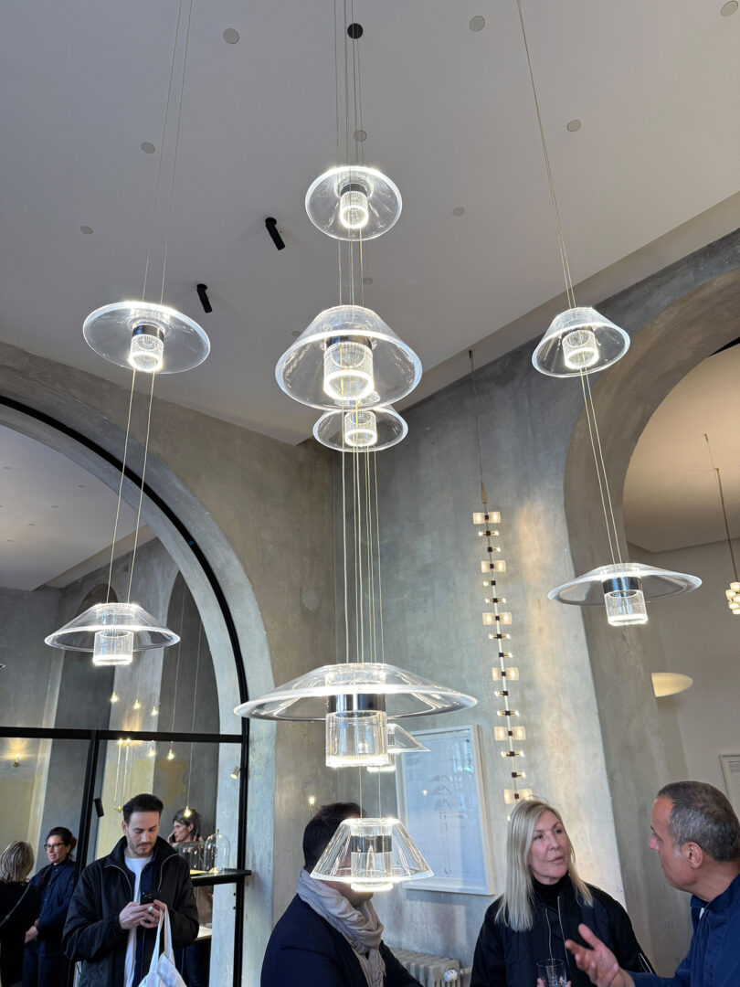 A modern, circular Aura Snøhetta pendant light fixture hangs from the ceiling, emitting a soft white glow against a dark background.