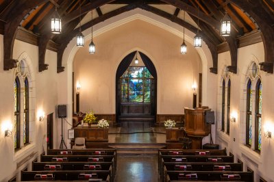 View of the interior of a chapel with a stained glass window at back. 