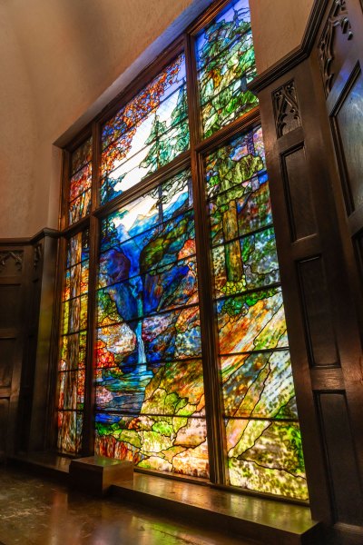 View of a monumental stained-glass window of a mountain landscape with highly saturated color. 