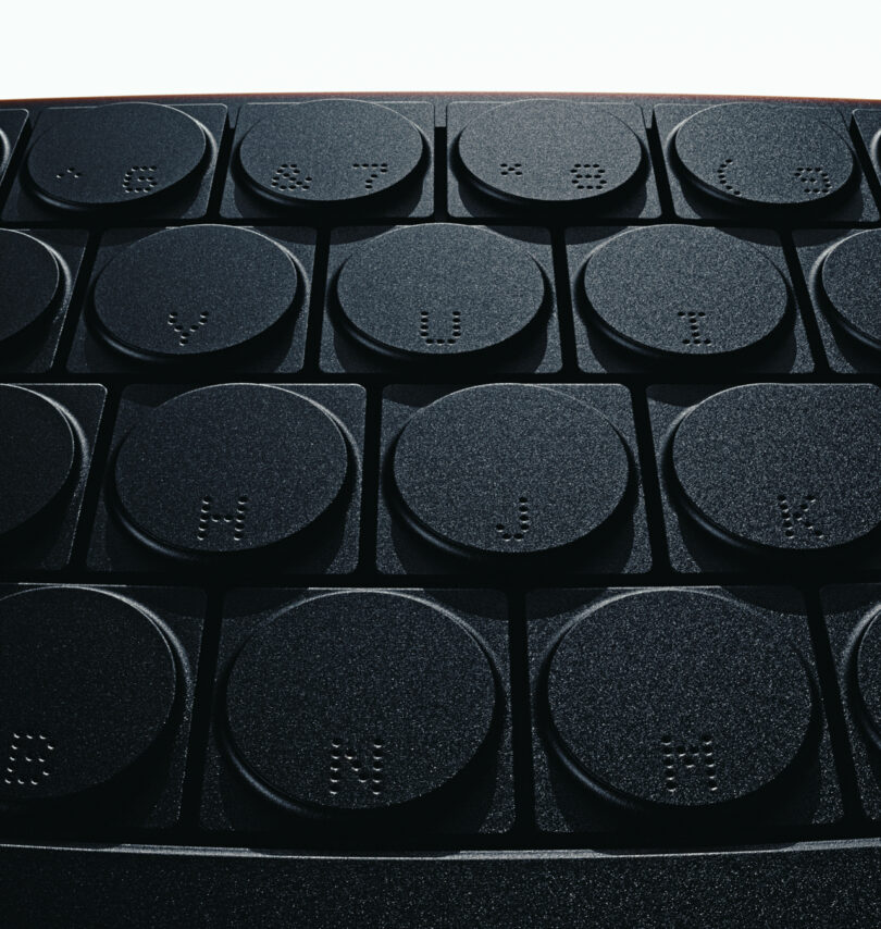 Close-up of a textured surface with multiple round black buttons, each featuring tactile Braille dots arranged in a grid pattern, resembling the precise layout of a cleaver’s edge.