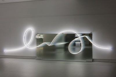 A squiggle-shaped neon lighting tube above a mirror.