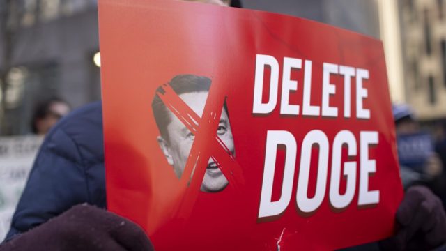 After-two-court-losses-DOGE-asks-Supreme-Court-for-Social.jpg A protestor holds a sign that has a picture of Elon Musk with an X over his face, and text that says "Delete DOGE"