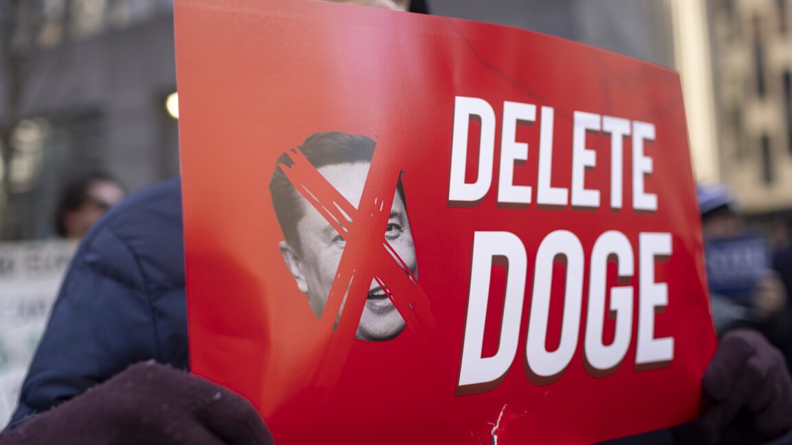 After-two-court-losses-DOGE-asks-Supreme-Court-for-Social.jpg A protestor holds a sign that has a picture of Elon Musk with an X over his face, and text that says "Delete DOGE"