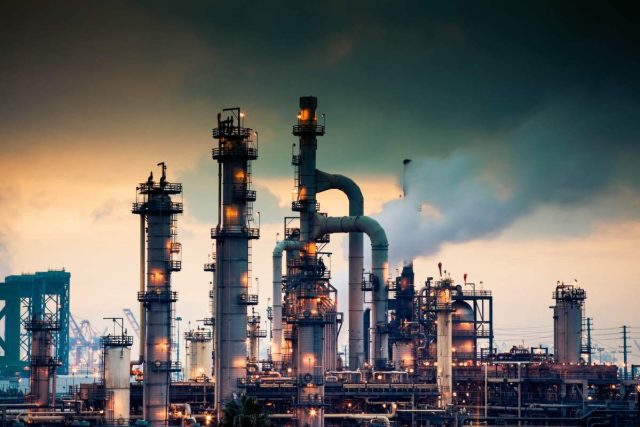 Ara-Partners-new-800M-fund-will-decarbonize-old-industrial-assets.jpeg A steaming, glowing mass of smoke stacks and distillation towers connected by conduit and pipe racks towers in the early morning light in front of the Port of Los Angeles.