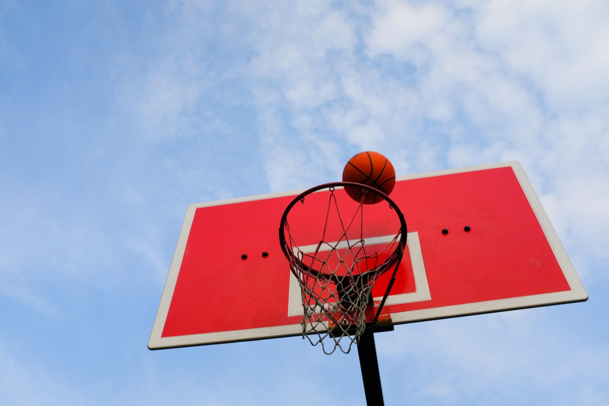 a basketball flies into the basket, against the blue sky, in an open area.