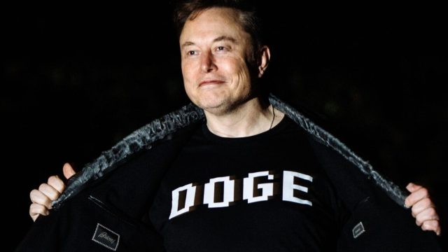 Elon-Musk-to-exit-government-upset-that-Trump-bill-undermines.jpg Elon Musk wearing a T-shirt with the word "DOGE" printed on the front.