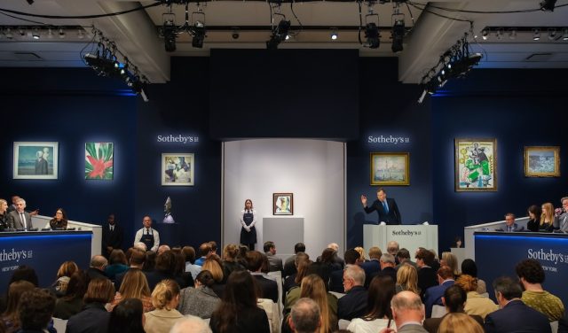 An auctioneer gestures before a crowded sales room.