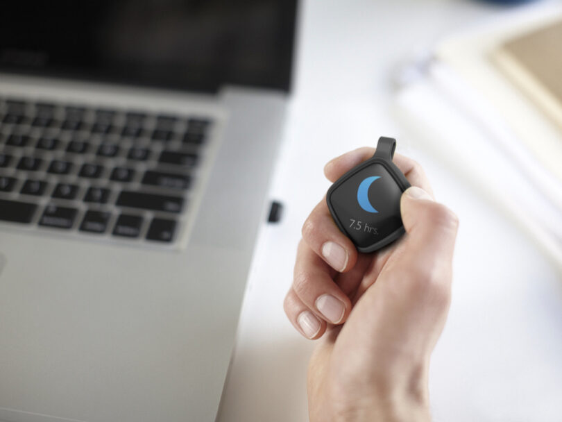 A hand holds a fitness tracker device showing a crescent moon icon and 