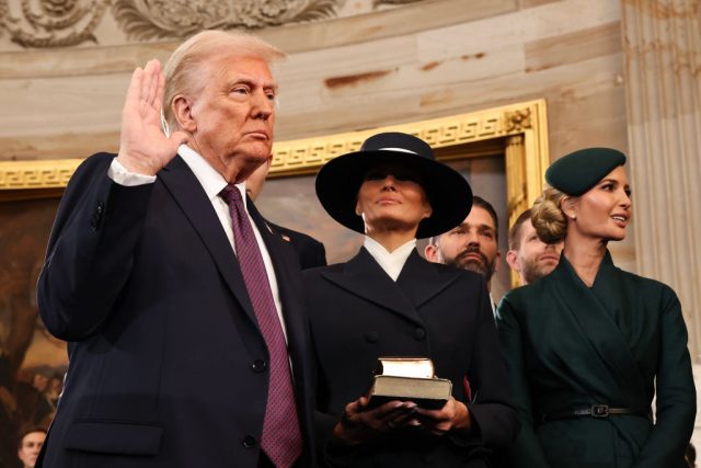 Major-Art-Patrons-Donated-Millions-to-Trump-2025-Inauguration-Report.jpg A suited man holds his right hand up next to two smartly dressed women.