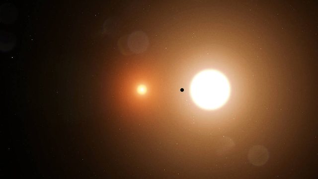 New-data-confirms-There-really-is-a-planet-squeezed-in.jpeg Image of two stars, one small and a dull orange, one larger and a bright yellow. In between is a small dark object.