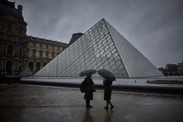 Rain-Leaks-Into-Louvres-Cimabue-Exhibition.jpg Two people shelter under an umbrella during a rainy day next to a glass pyramid structure.